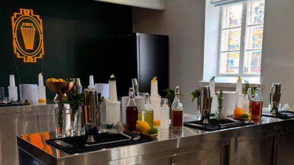 Kuvassa näkyy rosteriset baaritiskit, joiden päällä on laajalti drinkkikoulussa käytettäviä miksereitä, baarimikon työvälineitä sekä tarvikkeita. Drinkkikoulutus Helsinki on pitopaikkana.